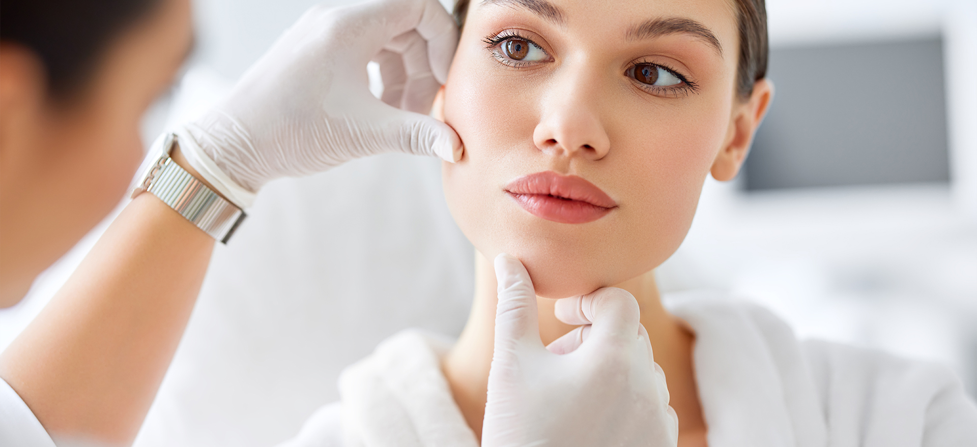 A gloved practitioner assessing a client's jawline during a consultation.